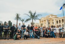Programa Paraíba sem Fronteiras oferece 25 vagas para graduação no Reino Unido A diverse group poses outdoors in front of a historic building with palm trees.