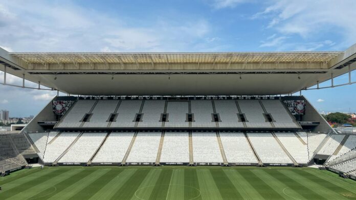 s4-84a1854042d1-9 Wide view of an empty football arena in São Paulo, featuring a green pitch under a sunny sky.