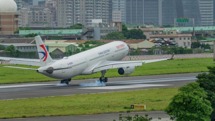 s4-84e906cfe67e-4 A China Eastern airplane landing on a runway with a city skyline in the background.