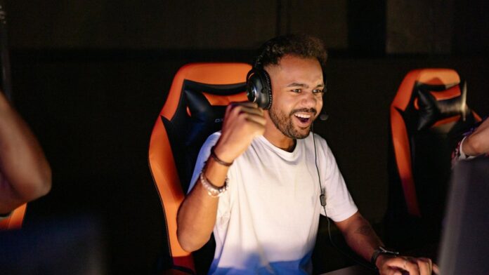 s4-85d0da2567d3 A man celebrating a win in a gaming chair, wearing headphones and using a PC.