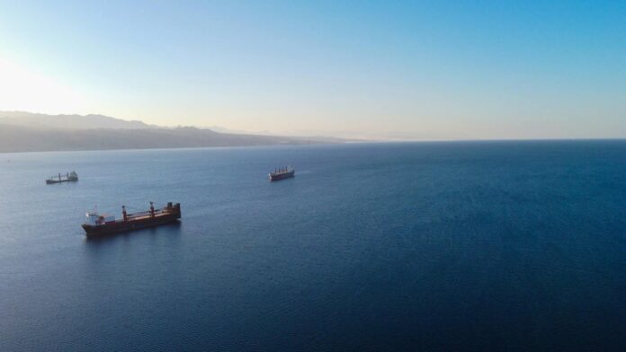 An aerial view of cargo ships sailing on a tranquil ocean with a clear blue sky.