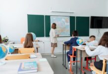 Fiscalização da educação garante eficácia de políticas públicas Students engaged in a geography lesson, focusing on a wall map in a classroom with globes and study materials.