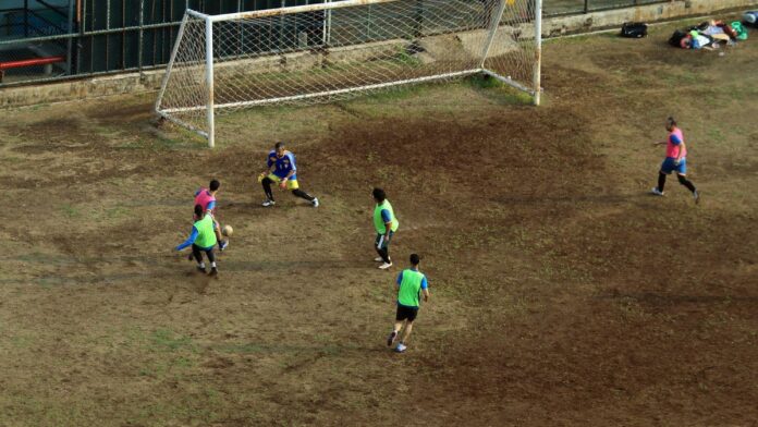 Players engaged in a soccer match on a muddy field, viewed from above.