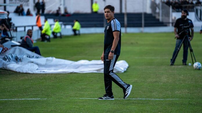 Soccer coach in athletic attire watching the game on a grassy field.
