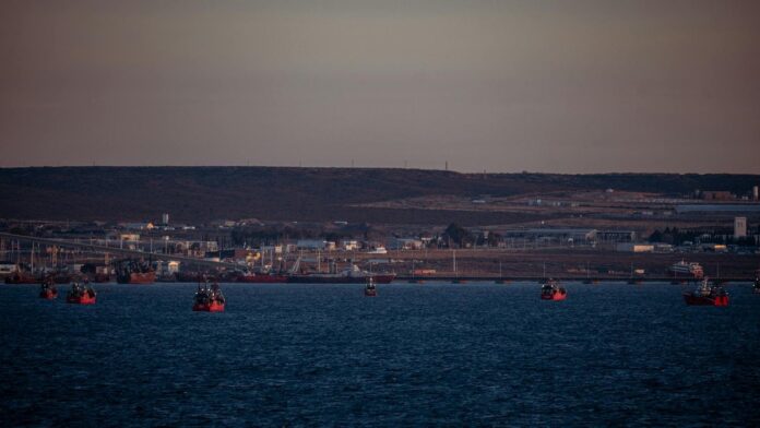 Distant view of fishing boats in a harbor at sunset with an industrial backdrop.