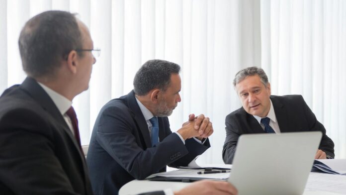s4-ac18e2ec16c0 Three businessmen collaborating during a meeting around a laptop in a bright office.