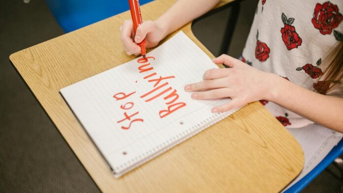 s4-ad2414a1266f-2 A child writes 'Stop Bullying' in a notebook on a school desk, promoting awareness.