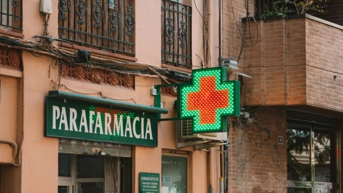 A street view of a parafarmacia with a glowing neon cross, showcasing urban pharmacy architecture.