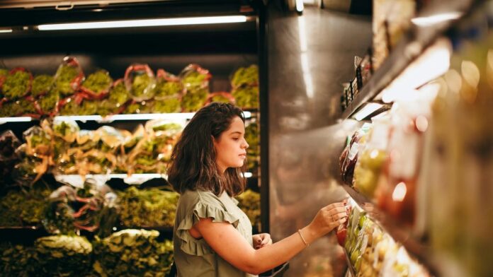 A woman selecting fresh vegetables from a supermarket aisle.
