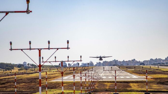 An airplane lands on the runway at Londrina Airport, Brazil, with cityscape in background.