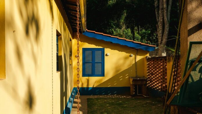 Sunlit yellow house exterior with blue accents in rural Brazil setting.