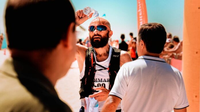 A male runner cools down with water during a summer marathon by the seaside.