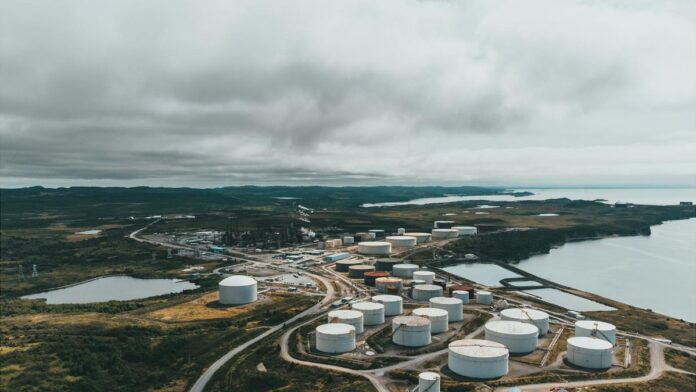 Aerial landscape shot of a coastal oil refinery with storage silos under cloudy skies.