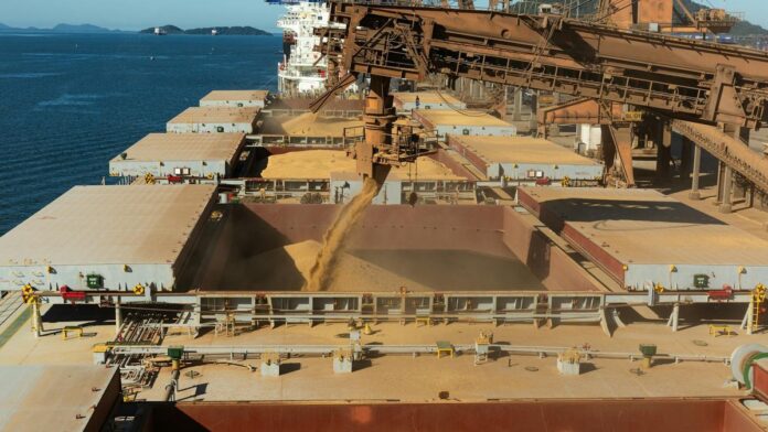 Aerial view of a cargo ship loading grain at a bustling industrial port by the sea.