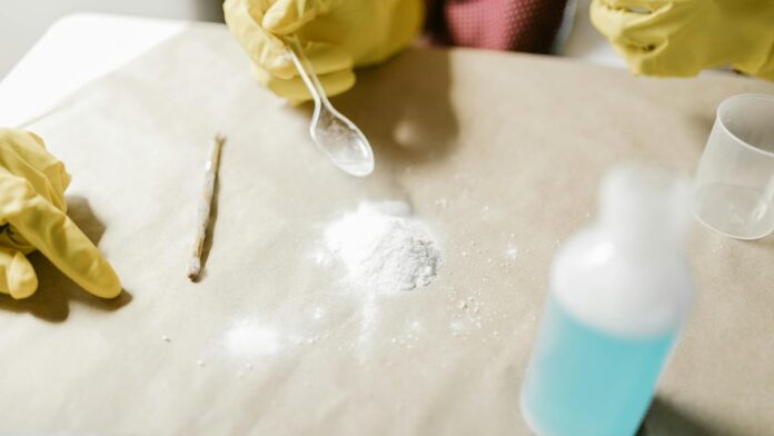 s4-bf23ce05ebf4 Close-up of a science experiment with yellow gloves, powder, and blue liquid indoors.