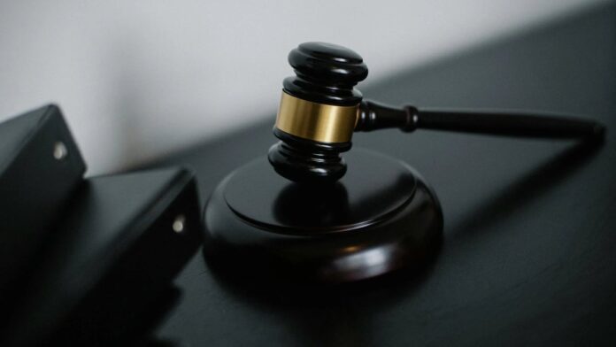 High angle of shiny wooden ceremonial mallet with golden detail placed on judge tale near documents folders