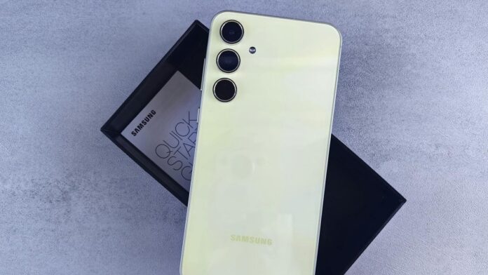 Yellow Samsung smartphone displayed on a gray surface with its box and quick start guide.