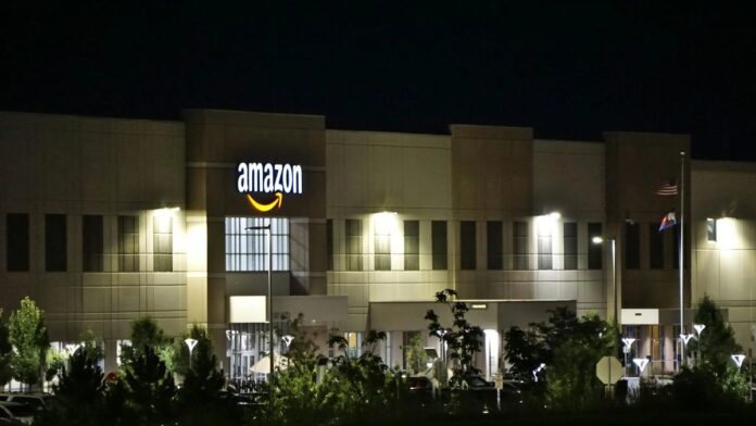 Amazon warehouse building illuminated at night with trees and signage.