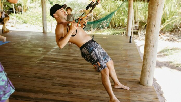 Fit man performing TRX workout on a wooden deck with tropical backdrop, showcasing outdoor exercise and healthy lifestyle.