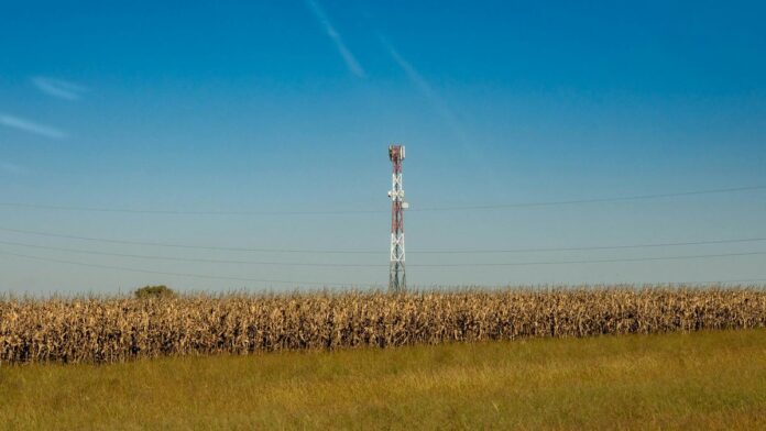 A communication tower in a rural field with a clear blue sky.