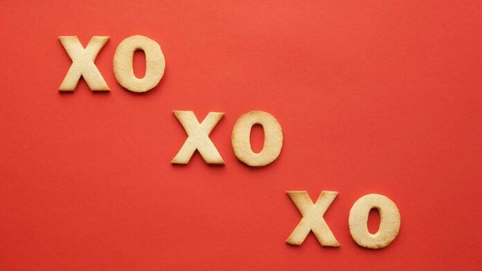 Flatlay of XO shaped cookies arranged on a vibrant red background, perfect for Valentine's theme.