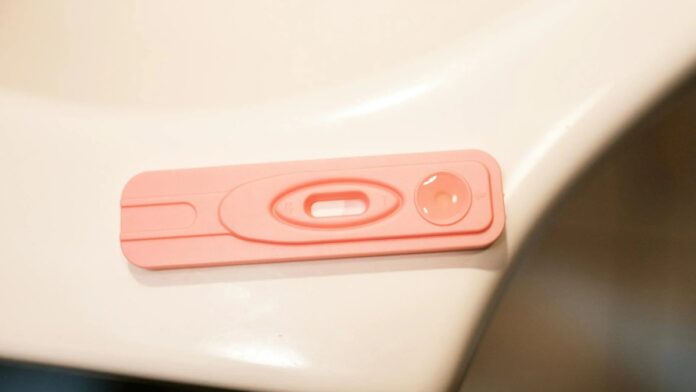 A detailed close-up of a pink pregnancy test kit on a white surface.