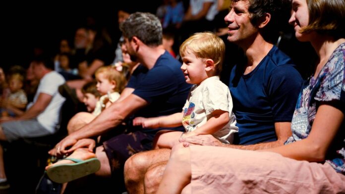 A diverse audience, including families, enjoys a live performance in a Brasil theater.