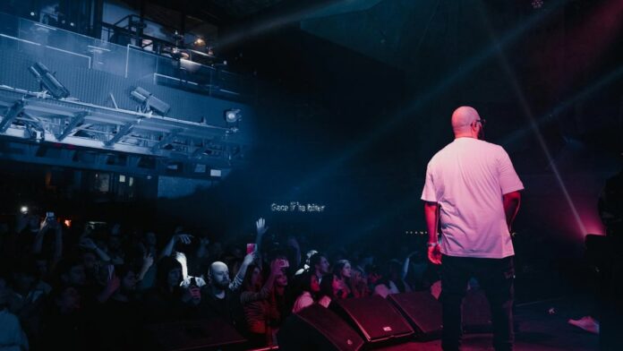 Rapper performing live on stage with vibrant lighting and engaged audience in a concert setting.