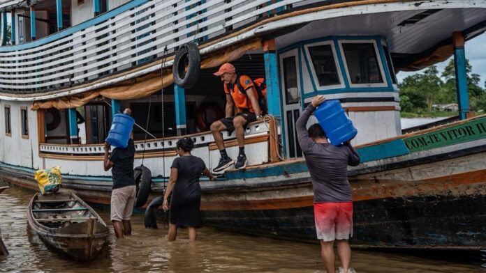 Funcionários da Saneacre realizando manutenção em tubulação de água às margens do Rio Juruá com nível elevado.