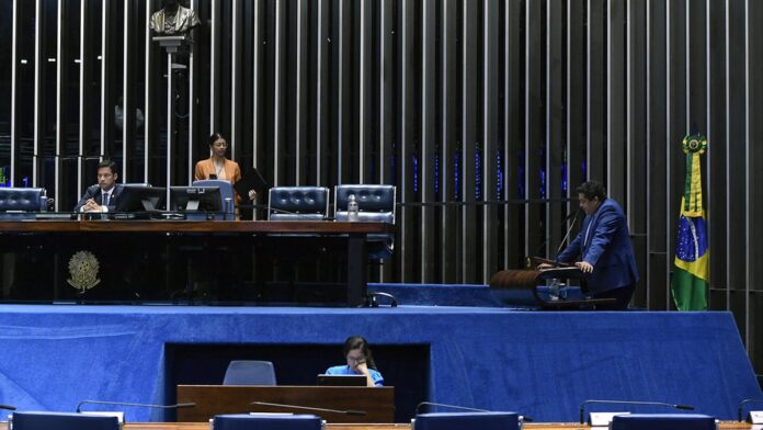 sine-pb-abre-361-vagas-de-emprego-em-11-munic-pios Atendente atende candidato em balcão de agência de empregos, com computadores e currículos sobre a mesa.