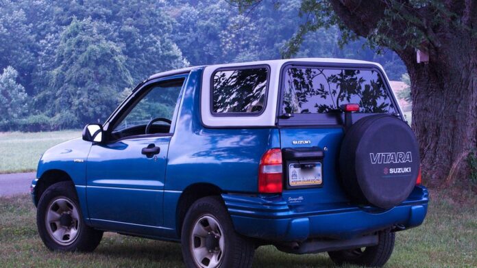 SUV Suzuki Vitara estacionado em via urbana, exibindo design robusto, grade frontal cromada e carroceria bicolor.