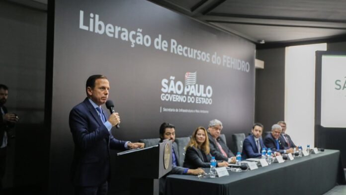 Pessoa segurando uma fatura de água próxima a um hidrômetro em ambiente residencial iluminado.