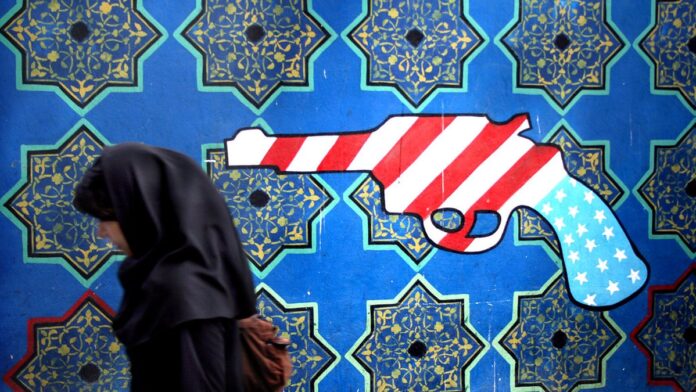 Diplomata iraniano falando em um pódio diante de bandeiras do Irã, simbolizando rejeição política e tensões diplomáticas.