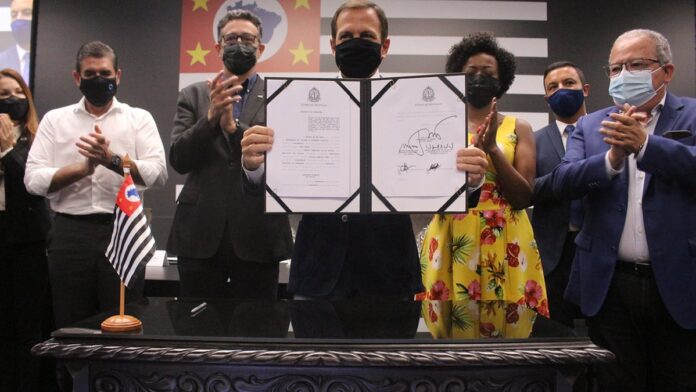 Jovens músicos de São Paulo e Buenos Aires cantam e gesticulam juntos em um estúdio com luzes coloridas ao fundo.