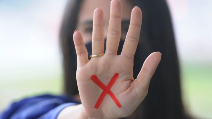 Mulher exibe a palma da mão aberta com o polegar dobrado, gesto que sinaliza pedido de socorro contra violência.