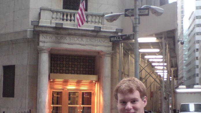 Painel digital da Bolsa de Valores de Nova York exibindo números verdes em alta com ícones de gráficos financeiros.